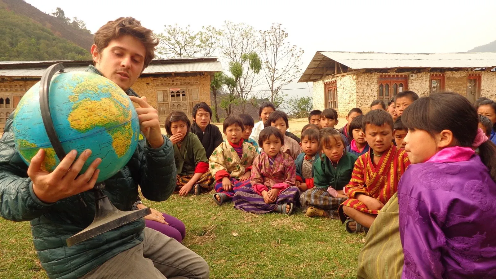 Dan Cordaro holding a globe for a circle of schoolchildren outside a school in Eastern Bhutan