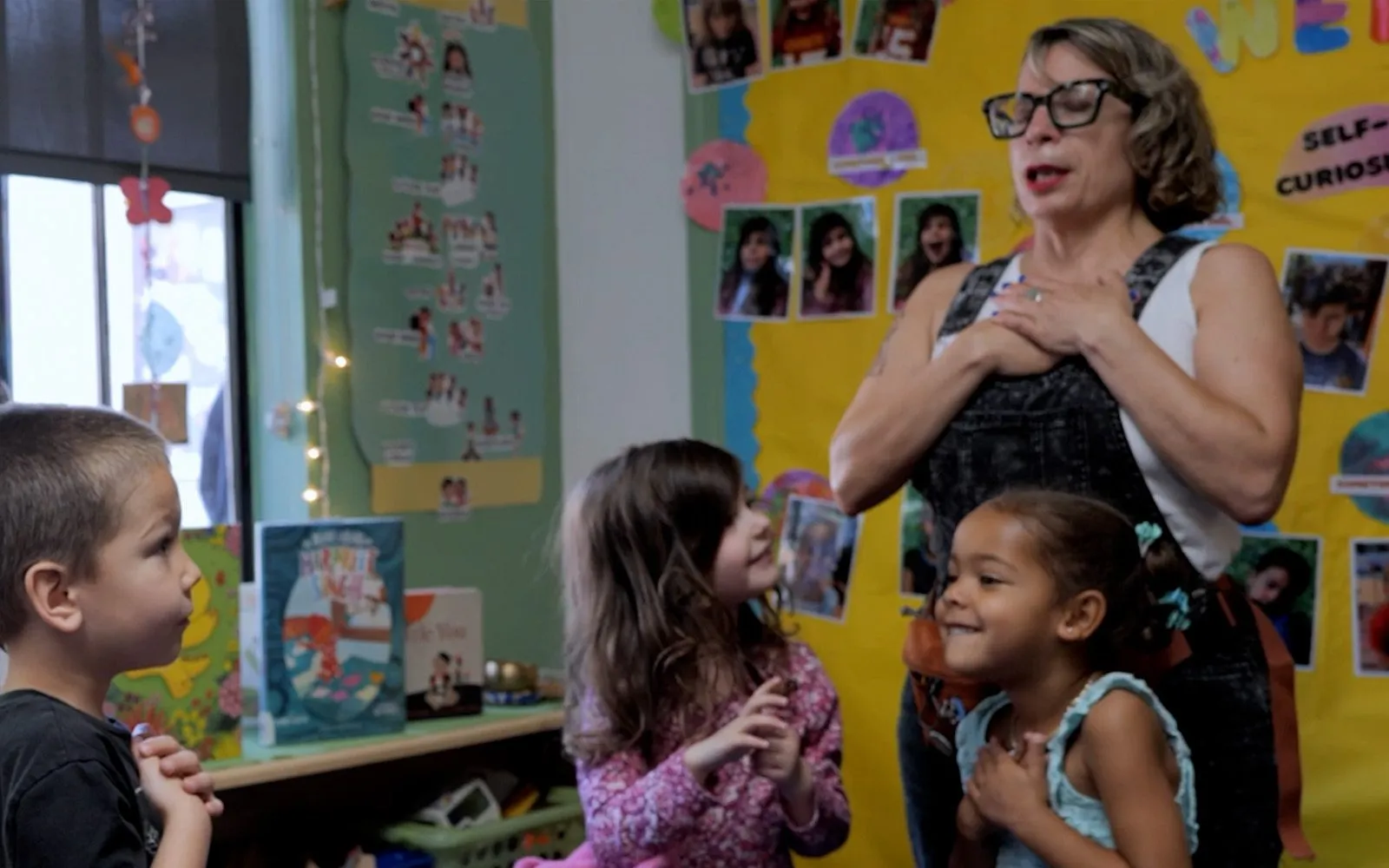 A teacher and her young students standing together with hands on their hearts in a classroom