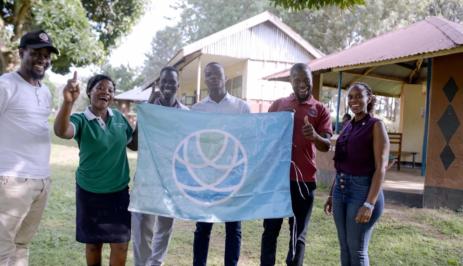 Educators holding The Contentment Foundation flag together outside a school in Uganda